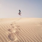 Mujer saltando en el aire sobre dunas de arena, España - foto de stock