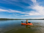 Garçon kayak sur le lac sous un ciel bleu nuageux — Photo de stock