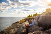 Boy sitting on rocks by a lake, Lake Superior Provincial Park, Estados Unidos — Fotografia de Stock