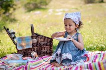 Улыбающаяся девочка, сидящая на одеяле для пикника в парке с пустой тарелкой, Болгария — стоковое фото