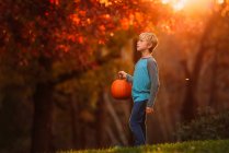 Boy standing in a garden carrying a pumpkin, United States — Stock Photo