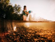 Chica de pie en un lago vaciando un cubo de agua, Lago Superior, Estados Unidos - foto de stock