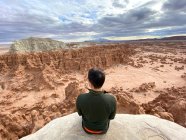 Visão traseira de um homem sentado na borda do penhasco, Goblin Valley State Park, Utah, EUA — Fotografia de Stock