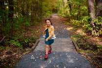 Chica corriendo a través de un pequeño puente en un sendero en un bosque, Estados Unidos - foto de stock