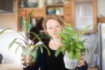 Femme debout dans la cuisine tenant deux plantes en pot — Photo de stock