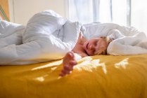Garçon couché au lit se réveillant — Photo de stock