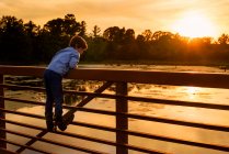 Хлопчик, що вилазить на поручні моста на заході сонця (США). — стокове фото