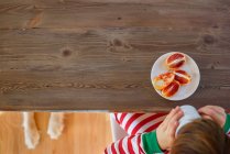 Overhead view of young boy having a snack with dog sitting underneath the table — Stock Photo