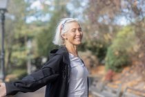 Smiling senior woman in park with arms outstretched — Stock Photo