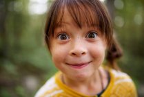 Portrait d'une fille avec des taches de rousseur debout dans la forêt tirant des visages drôles, États-Unis — Photo de stock