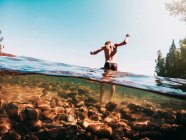 Вид сзади на мальчика, идущего по скалам в озере, США — стоковое фото