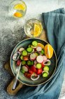 Deux verres d'eau de citron et un bol de concombre, tomate, oignon rouge et salade de radis — Photo de stock