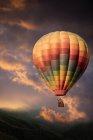 Hase und Reh in einem bunten Heißluftballon, der über Hügel in Richtung stürmischen Himmels steigt — Stockfoto