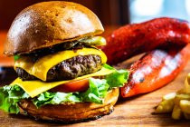 Close-up de um cheeseburger com tomate, pepino e alface servido com batatas fritas e pimentas vermelhas assadas — Fotografia de Stock