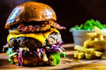 Gros plan d'un hamburger texan avec salade de fromage, bacon et chou servi avec des chips sur une planche à découper en bois — Photo de stock