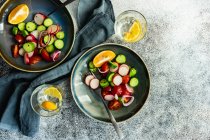 Copos de água com limão e taças de pepino, tomate, cebola vermelha e salada de rabanete — Fotografia de Stock