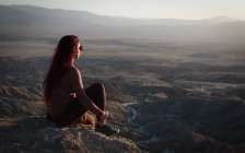 Mujer sentada en la montaña mirando las tierras baldías vista de la montaña, Anza Borrego Desert State Park, California, EE.UU. - foto de stock