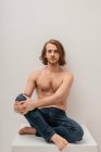 Portrait d'un bel homme torse nu en jeans assis sur une table — Photo de stock
