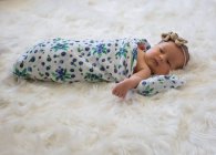 Новорожденная девочка, завернутая в одеяло, лежит на пушистом белом ковре — стоковое фото