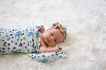 Newborn baby girl wrapped in blanket lying on fluffy white rug — Stock Photo