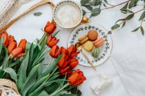 Чашка кофе и макароны с красными цветами тюльпан за столом — стоковое фото