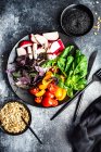 Healthy food concept with raw vegetables and herbs on black ceramic plate with seeds on dark stone background — Stock Photo