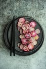 Органические свежие ломтики редьки на каменной тарелке с палочками для еды — стоковое фото