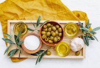 Bandeja de madera de cuencos con aceite de oliva y aceitunas con ramas sobre fondo blanco - foto de stock