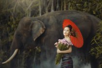 Beautiful woman holding a bunch of flowers standing by an elephant, Thailand — Stock Photo