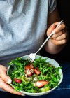 Женщина ест здоровый салат из руколы с клубникой и киви — стоковое фото