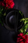 Ajuste de mesa asiático con tazón de cerámica negra y chopstics decorados con flores de peonía roja - foto de stock