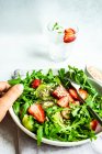 Healthy food concept with bowl full of fresh organic rucola salad with strawberry and kiwi on concrete background — Stock Photo