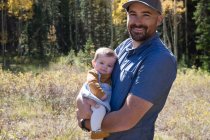 Portrait of a smiling man holding his baby daughter in the forest, California, USA — Stock Photo