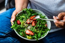 Женщина ест здоровый салат из руколы с клубникой и киви — стоковое фото