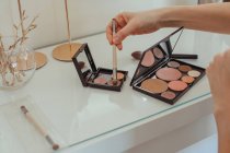Close-up of a woman's hand dipping a make-up brush in a make-up palette on a dressing table — Stock Photo