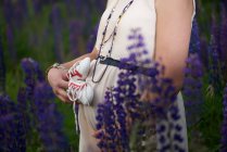 Close-up of a pregnant woman standing amongst flowers holding baby booties against her belly — Stock Photo