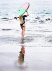 Rear view of a surfer walking into ocean carrying a surfboard above her head, Bahamas — Stock Photo