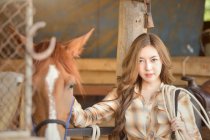 Portrait of a beautiful woman standing in a stable with her horse — Stock Photo