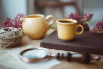 Une tasse de café sur une table avec une cruche à lait, loupe, ficelle et fleurs — Photo de stock