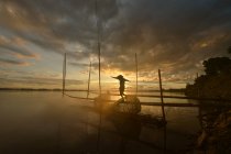 Silueta de un pescador caminando a lo largo de un embarcadero al atardecer, Tailandia - foto de stock