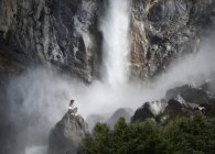 Mujer sentada en una roca en la base de Bridalveil Fall, Parque Nacional Yosemite, California, EE.UU. - foto de stock