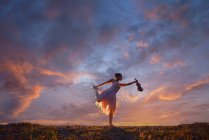 Woman standing outdoors on one leg holding a violin at sunset, Thailand — Stock Photo