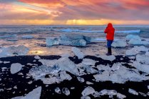 Vista traseira de uma mulher tirando uma foto ao pôr do sol, Diamond Beach, Jokulsarlon, Vatnajokull Glacier National Park, Islândia — Fotografia de Stock
