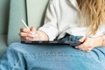 Mulher sentada em um sofá trabalhando em seu tablet — Fotografia de Stock