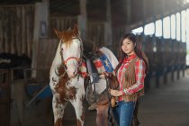 Femme debout dans une écurie avec son cheval prêt à monter — Photo de stock