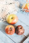 Zwei morsche Äpfel auf einem Tisch neben frischen reifen Äpfeln — Stockfoto