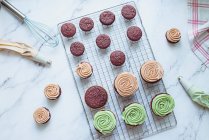 Overhead view of chocolate cupcakes with mint and coffee buttercream icing on a cooling rack — Stock Photo