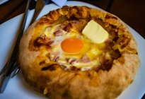 Adjarian khachapuri with cheese, ham, egg yolk and butter on plate with cutlery — Stock Photo