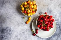 Bowls of red and yellow cherries on concrete surface, top view — Stock Photo