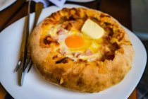 Adjarian khachapuri with cheese, ham, egg yolk and butter on plate with cutlery — Stock Photo